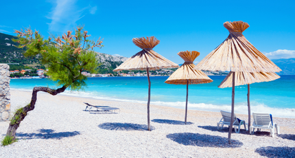 Kiezelstrand met parasols en helderblauw water op Krk in Kroatië
